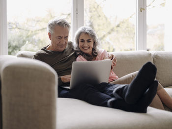 Happy senior couple with laptop relaxing on couch at home