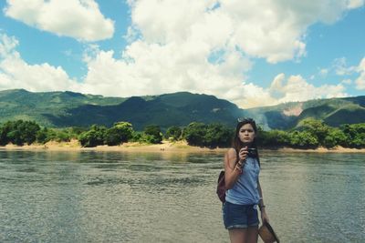 Young woman standing by lake against sky