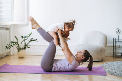 Young woman fit mom with baby girl doing fitness on mat at home