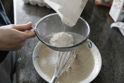 High angle of crop person sieving flour for cooking pastry in kitchen person