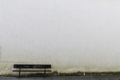 
the loneliness of a wooden bench on a white wall