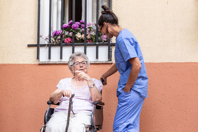 Happy senior woman with walking stick in wheelchair with her caregiver at home.