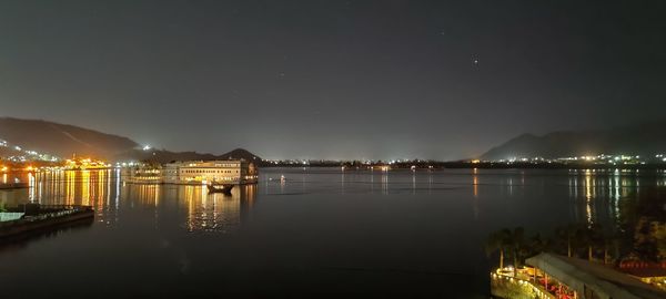 Illuminated city by lake against sky at night