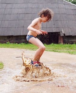 Full length of shirtless boy jumping in hug muddy puddle