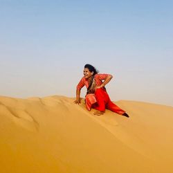 Woman on sand dune in desert against clear sky