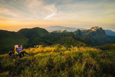 High angle view of woman sitting on cliff against mountains