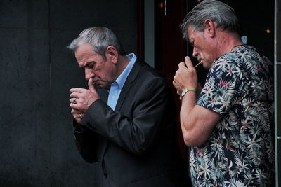 Men smoking cigarette by wall