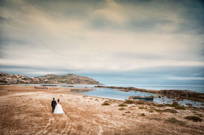 Rear view of wedding couple walking at beach during sunset