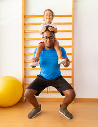 Father playing with his daughter holding her on his shoulders in the gym