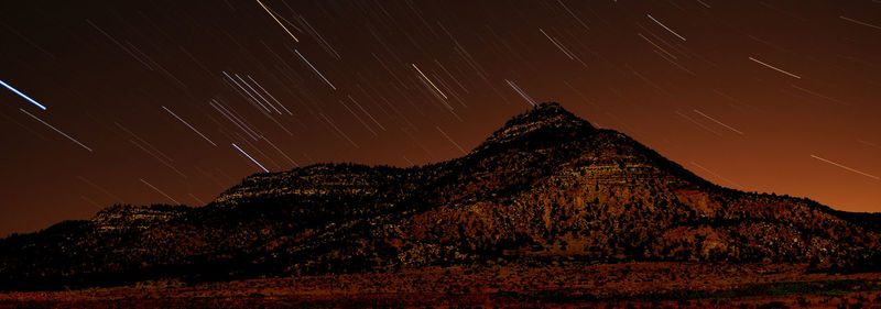 Panoramic view of star trails over mountains at night