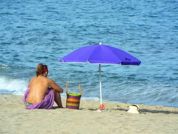 Rear view of seductive woman sitting at beach on sunny day