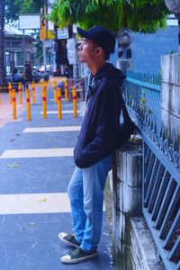 Side view of young man looking away while standing on footpath