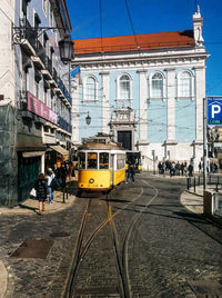 Tram on railroad track against buildings during sunny day