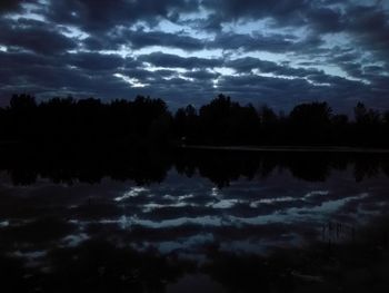 Reflection of silhouette trees in lake against sky