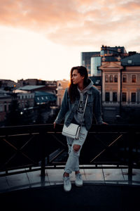 Young woman standing by railing against sky during sunset