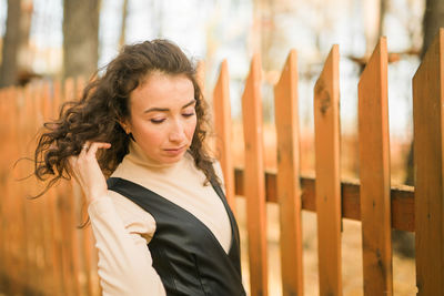 Portrait of young woman standing by fence