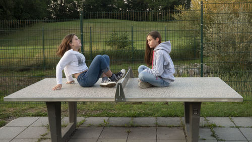 Woman sitting on bench against fence