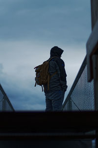 Rear view of man standing by railing against sky