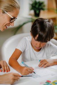 Child drawing shapes in a preschooler assessment test. psychologist helping him.