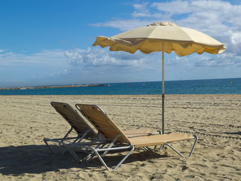 Deck chairs on beach against sky