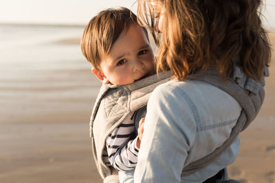 Mother carrying son while standing at beach