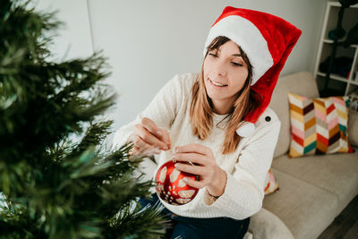 Smiling young woman standing by christmass tree at home