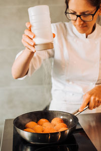 Female chef is sprinkle sugar on top of apricots to make confiture