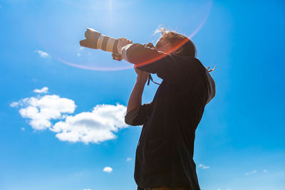 Low angle view of woman photographing against sky