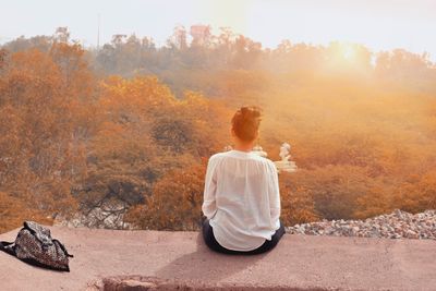 Rear view of woman sitting in autumn against sky