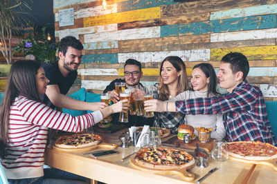 Happy friends toasting beer glasses while sitting at table in restaurant