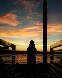 Rear view of silhouette man standing by sea against sunset sky