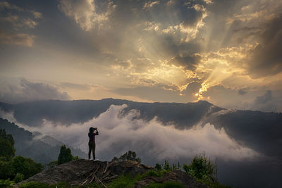 Woman standing on mountain against sky during sunset