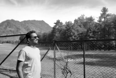 Man wearing sunglasses standing by railing against sky
