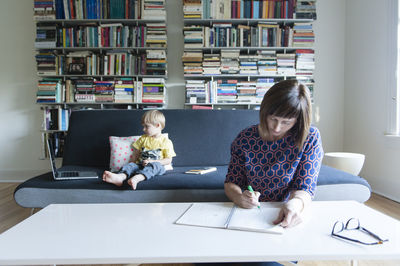 Mother writing while son looking laptop computer on sofa at home