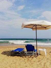 Deck chairs on beach against sky