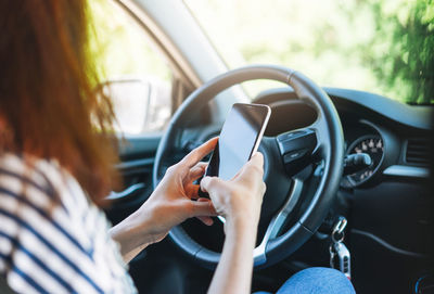 Crop photo of young woman driver using mobile phone in hands sitting in car in summer time