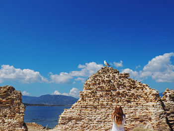 Rear view of woman standing on rock against sky