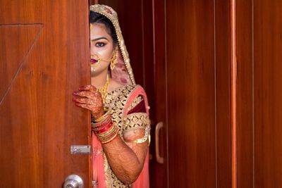 Portrait of woman in traditional clothing hiding behind door at home