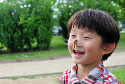 Close-up of cute boy with dragonfly on nose standing plants