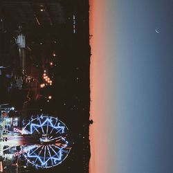 Illuminated ferris wheel by sea against sky at night