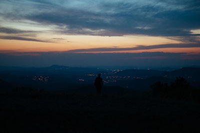 Silhouette person standing on landscape against sky during sunset