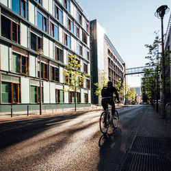 Rear view full length of man cycling on street by buildings