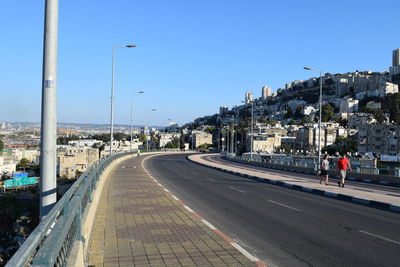 Road leading towards city against blue sky