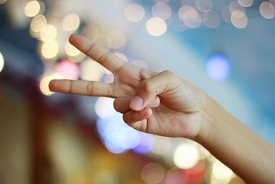 Cropped hand of woman gesturing peace sign against on illuminated lighting equipment