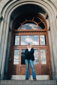 Full length portrait of young woman against building