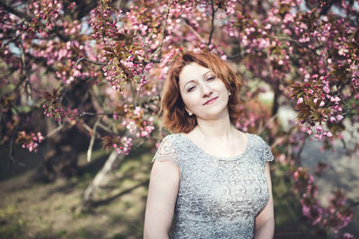 Cheerful middle aged armenian woman in elegant dress under the blooming sakura tree. spring season