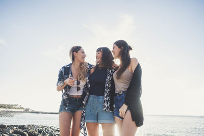 Friends standing at beach against sky