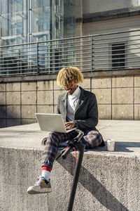 Man sitting on retaining wall using laptop