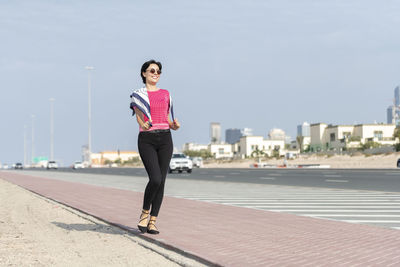 Full length of woman walking on sidewalk in city against sky