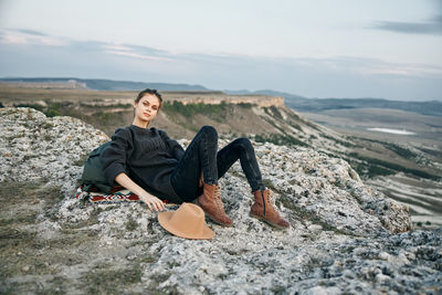 Portrait of woman sitting on rock against sky